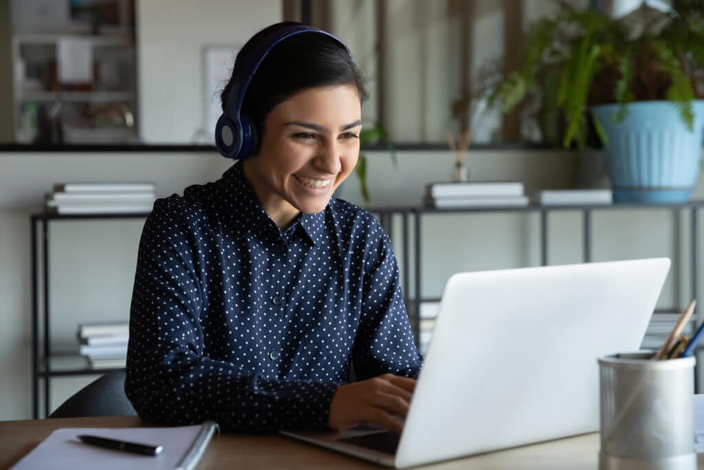 lachende Frau sitzt an Schreibtisch mit Headset und Laptop