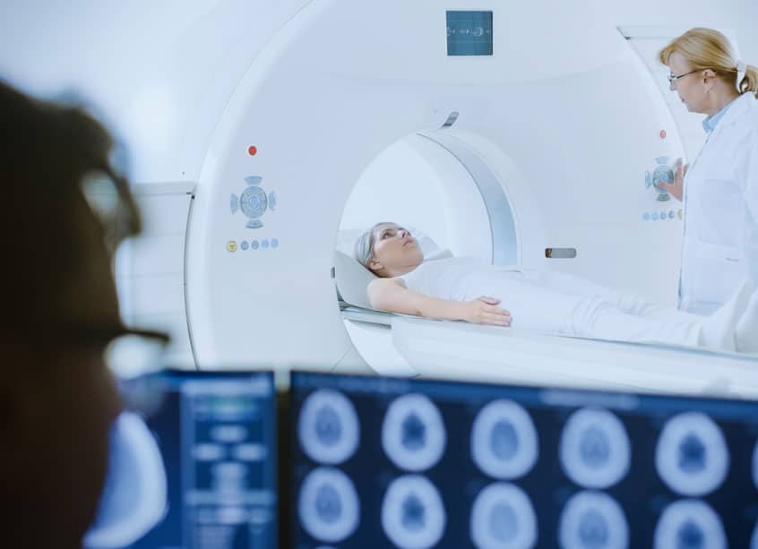 Frau Liegt im CT und wird von Ärztin und MTRA bei der Untersuchung begleitet