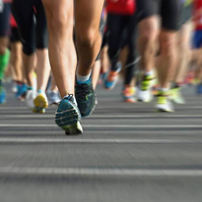 Füsse in Turnschuhen einer Gruppe von Läufern auf einer Asphaltstraße während einer Laufveranstaltung