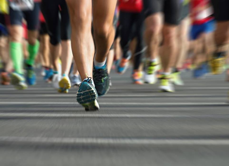 Füsse in Turnschuhen einer Gruppe von Läufern auf einer Asphaltstraße während einer Laufveranstaltung